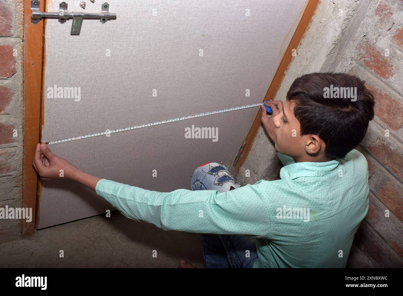 Teenage boy measures door size at home, wearing a light green shirt with black dots Stock Photo