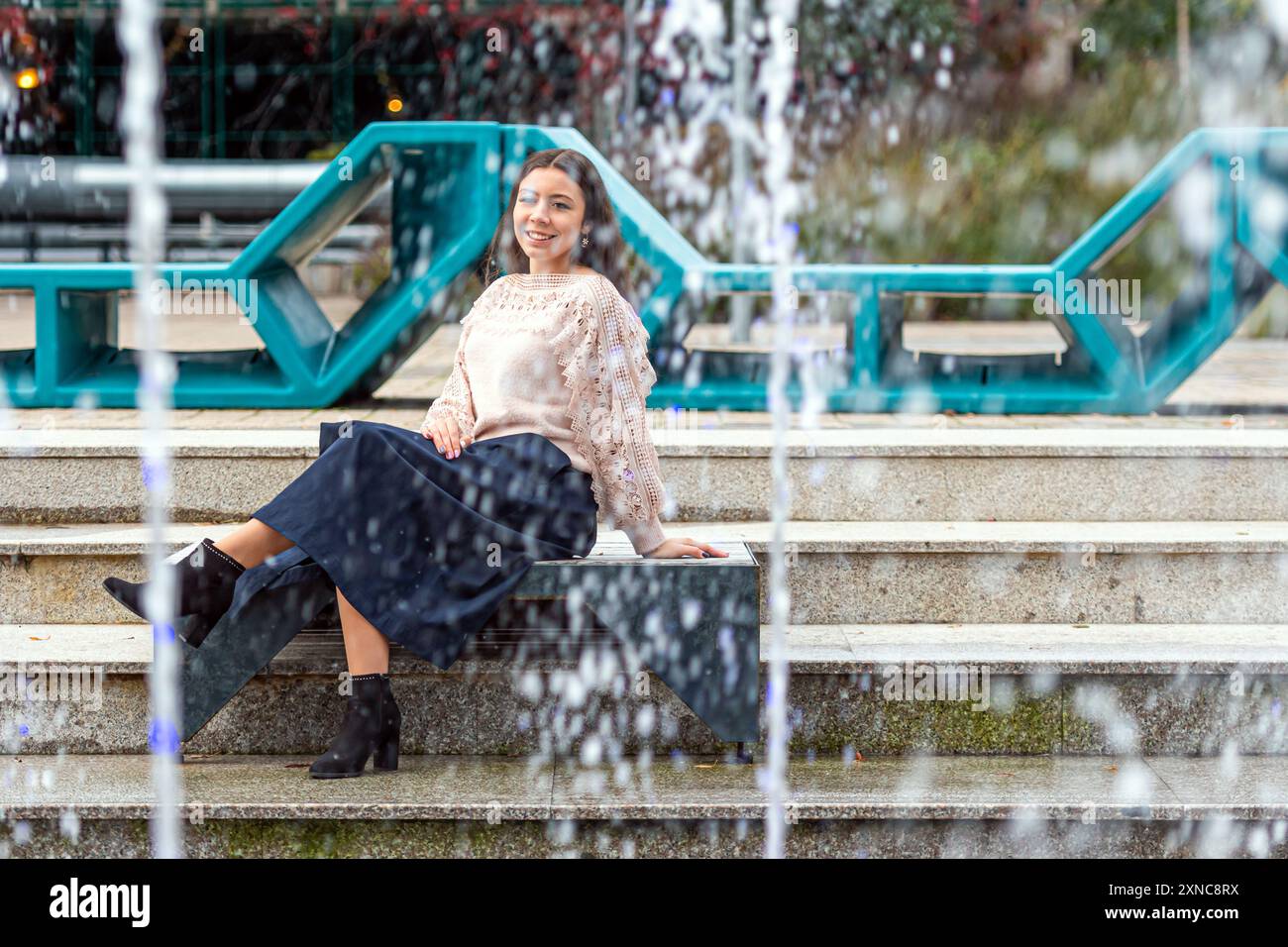 A young woman enjoys a peaceful moment beside a stunning fountain. Stock Photo