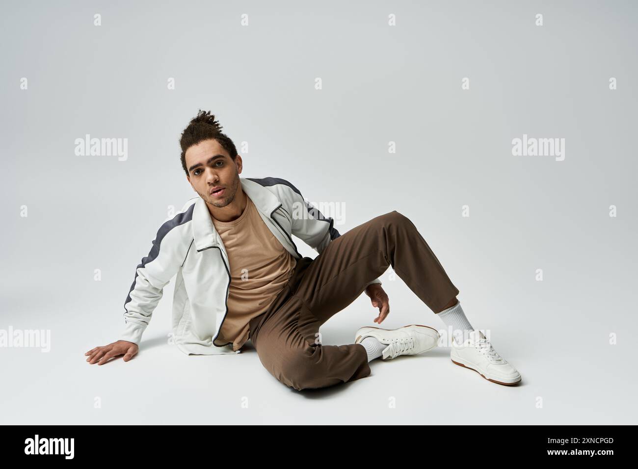 A young African American man in a stylish outfit poses against a grey ...