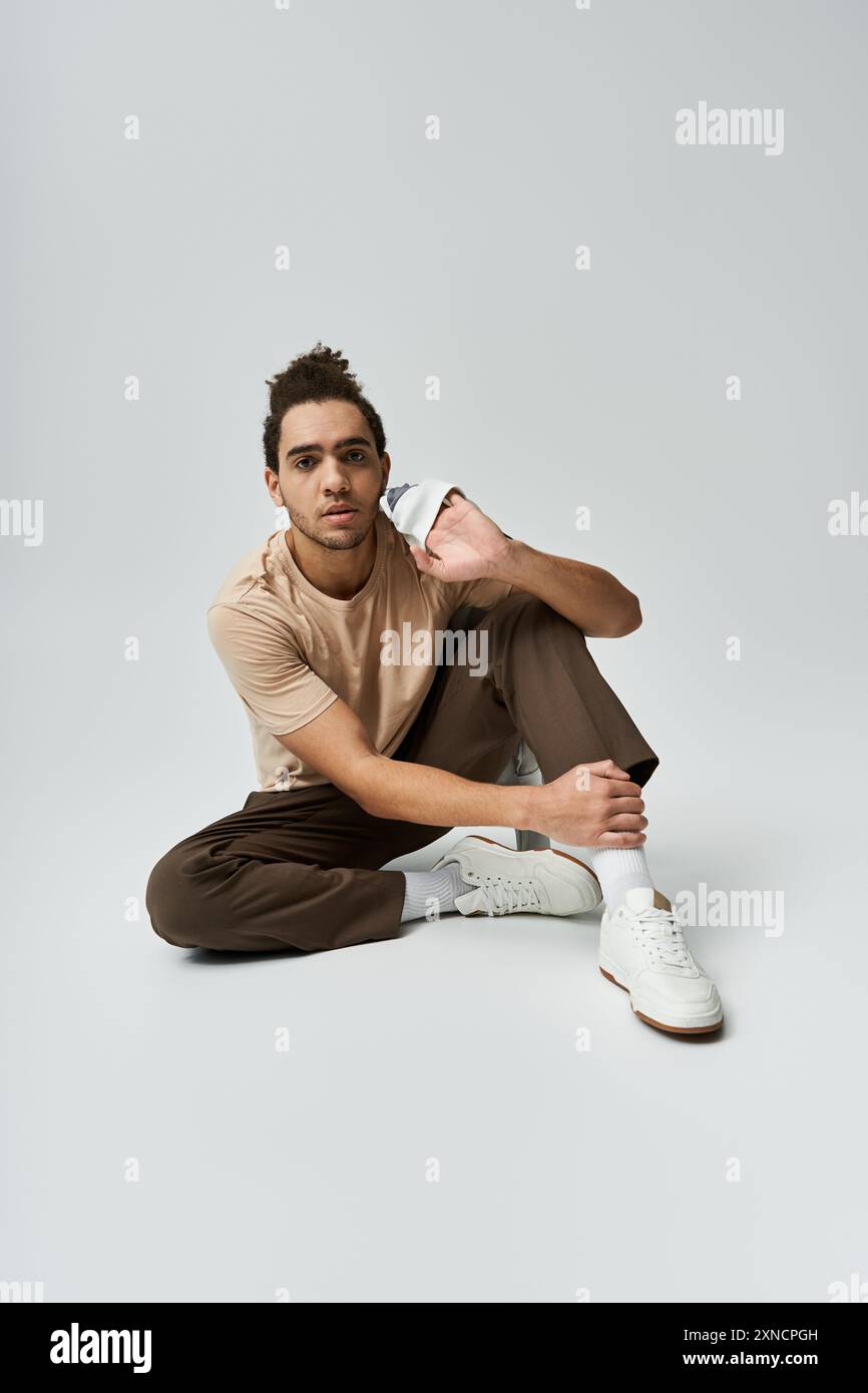 A young African American man in a stylish outfit sits casually on a ...