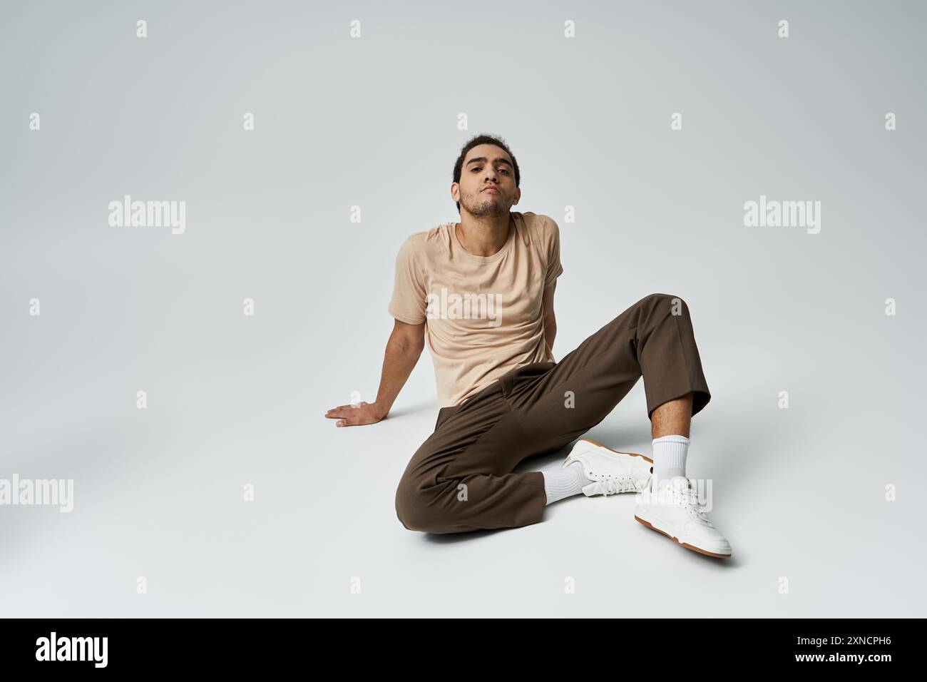 A young African American man in a stylish outfit poses on a grey ...