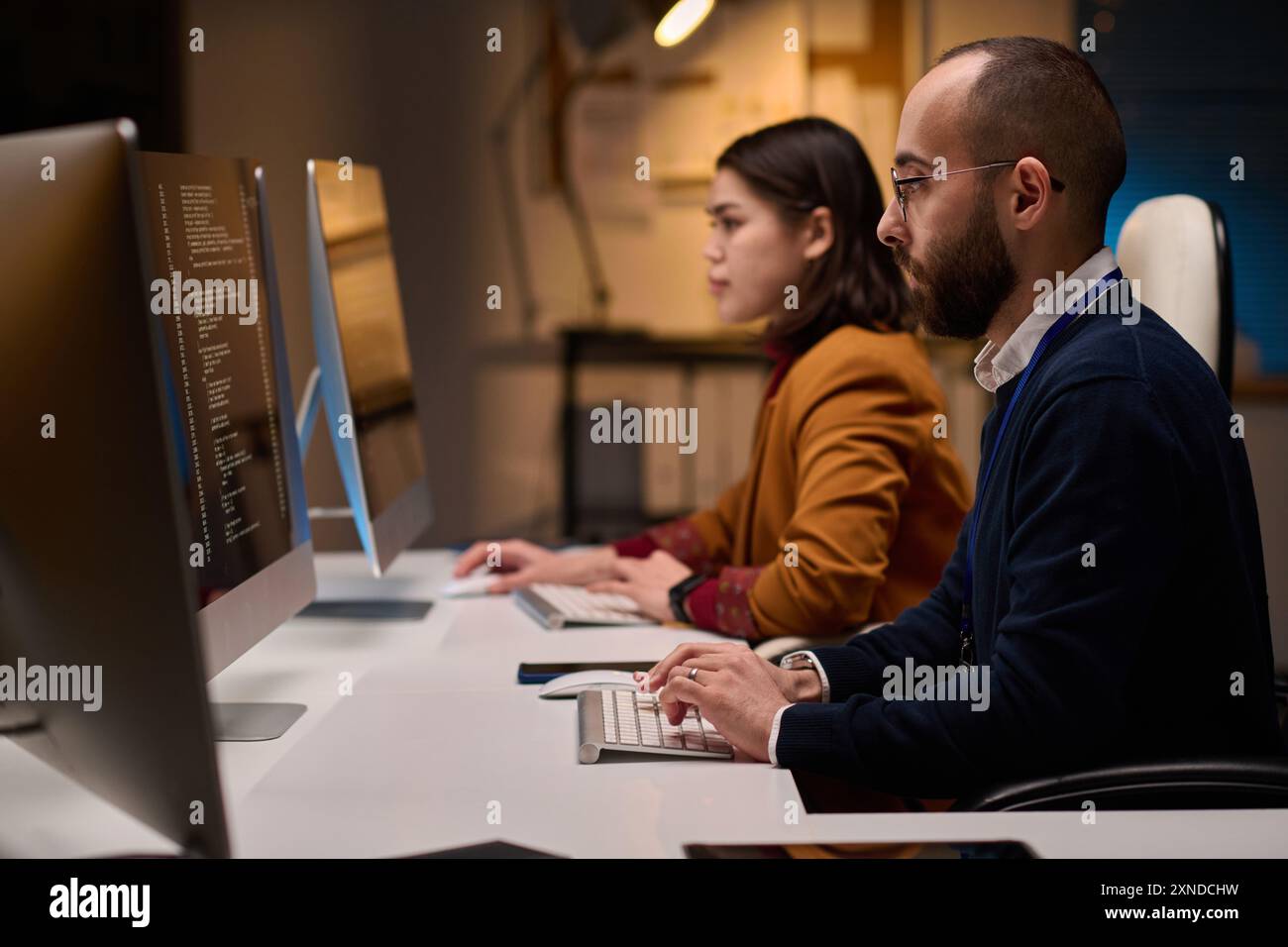 Side view portrait of two software developers using computers and writing code sitting at workplace in office Stock Photo