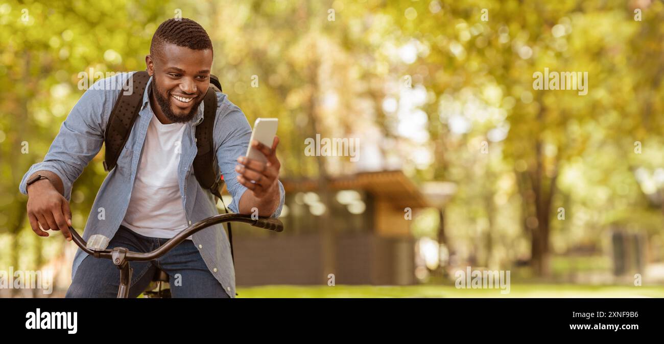 Happy Black Man Riding Bicycle Outdoors And Using Smartphone Stock Photo