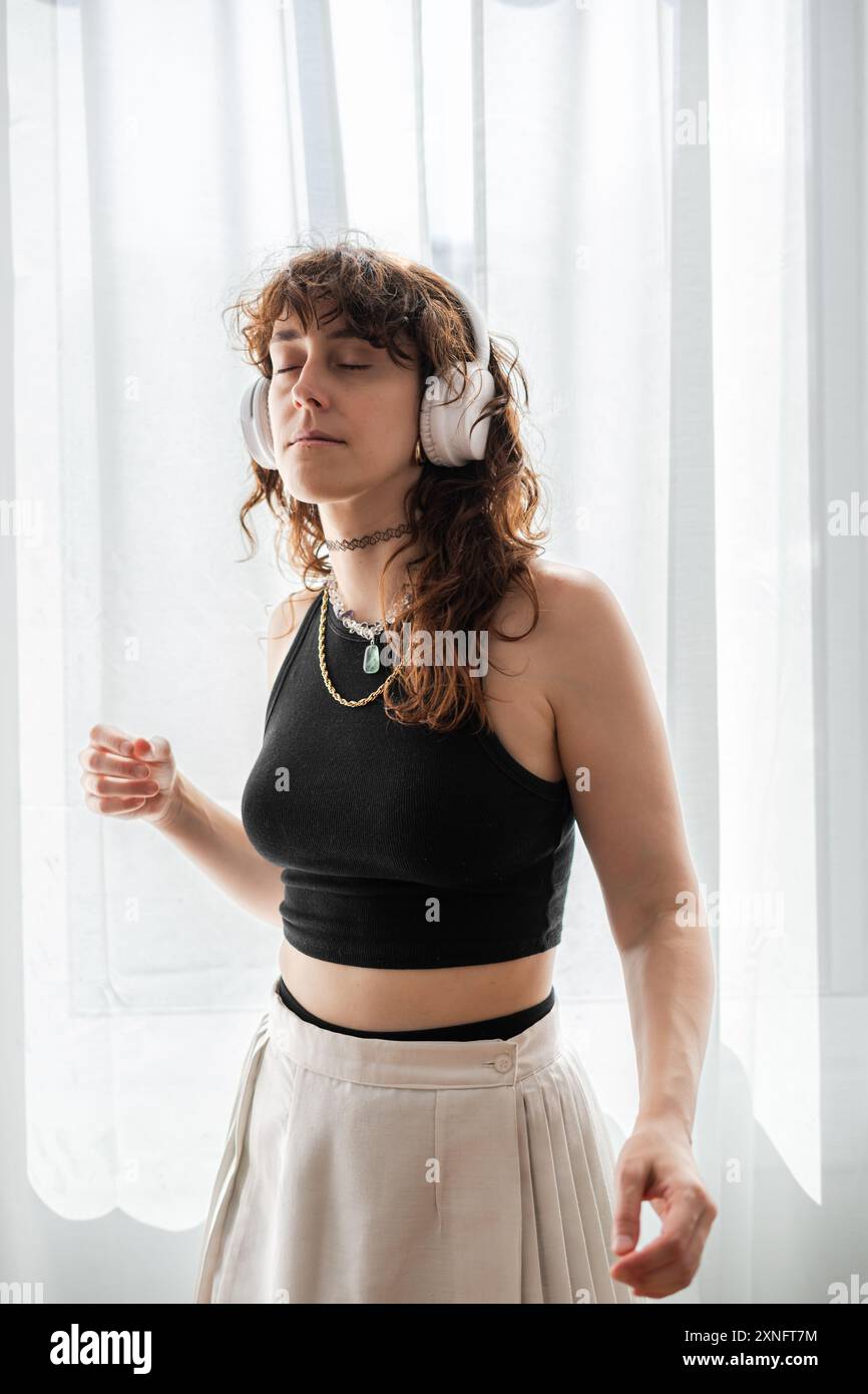 woman dances in front of the window while listening to music on her headphones. Stock Photo