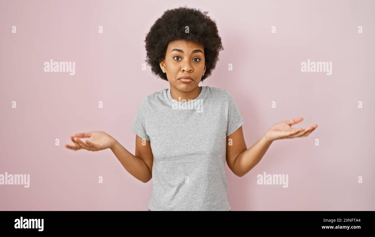 Curious african american woman with curly hair against pink background expressing uncertainty Stock Photo