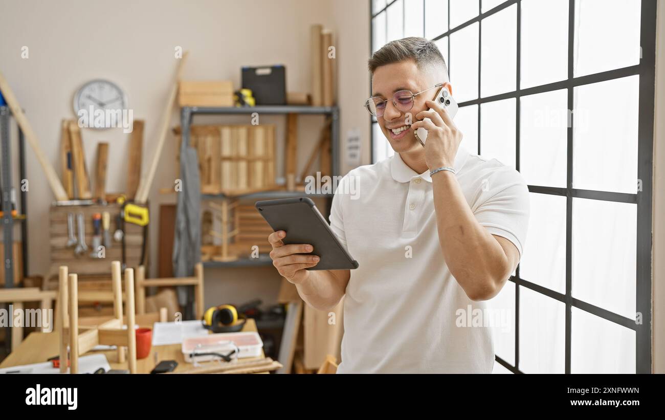 Smiling hispanic man using tablet and phone in a carpentry workshop Stock Photo