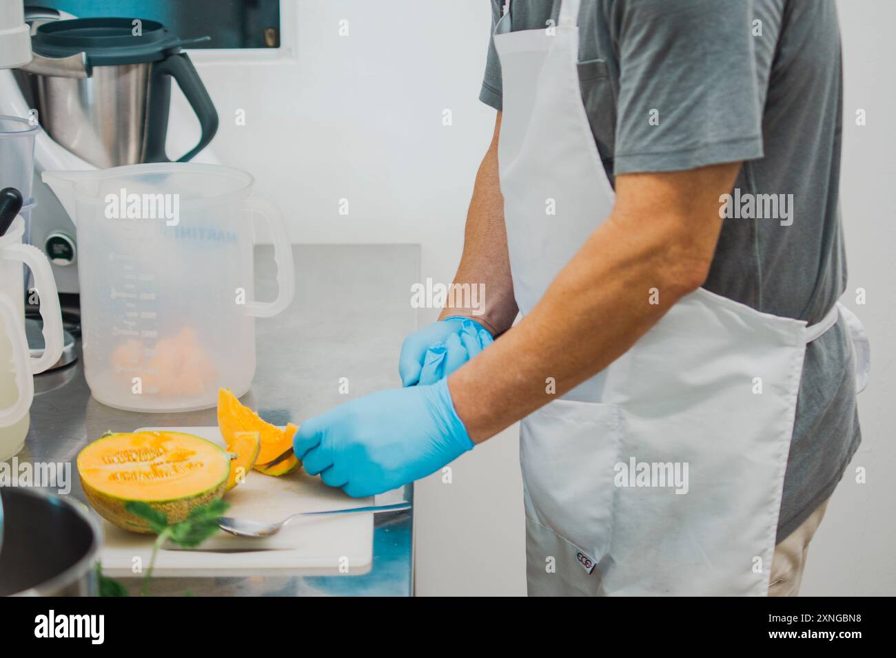 Chef in a modern kitchen prepares a fresh cantaloupe with precision and hygiene, showcasing professional skills in healthy food preparation Stock Photo