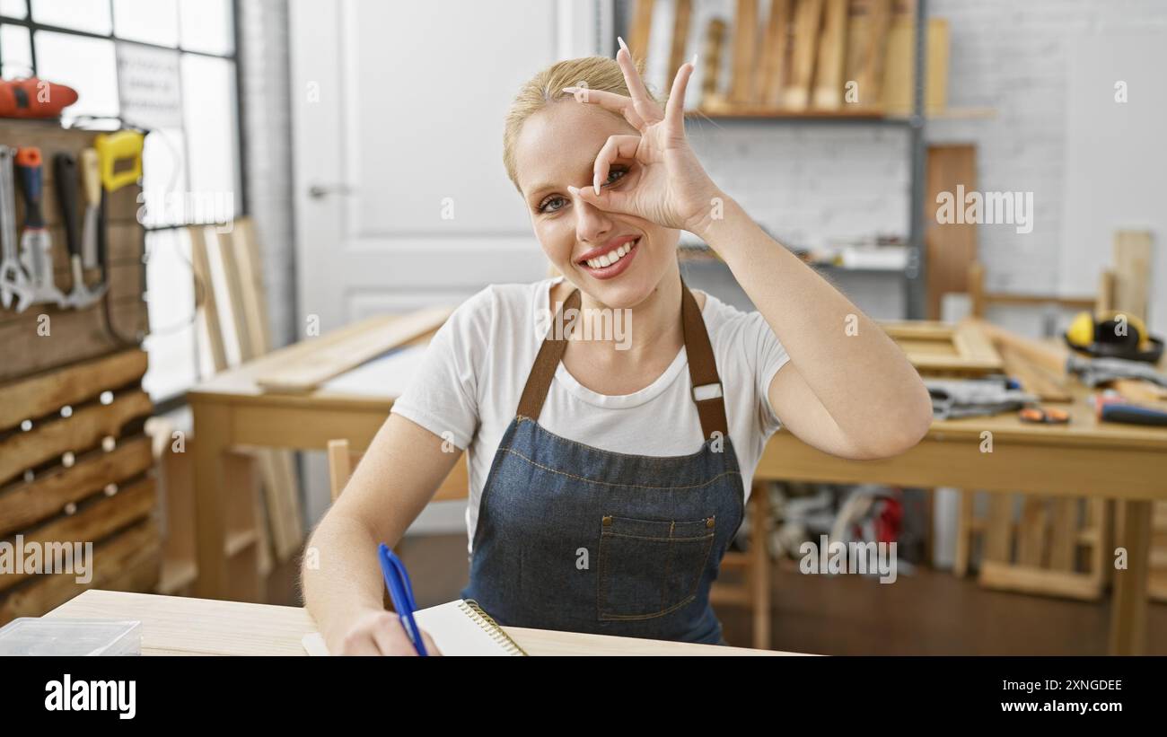 A smiling young woman with blonde hair wearing an apron makes an okay ...