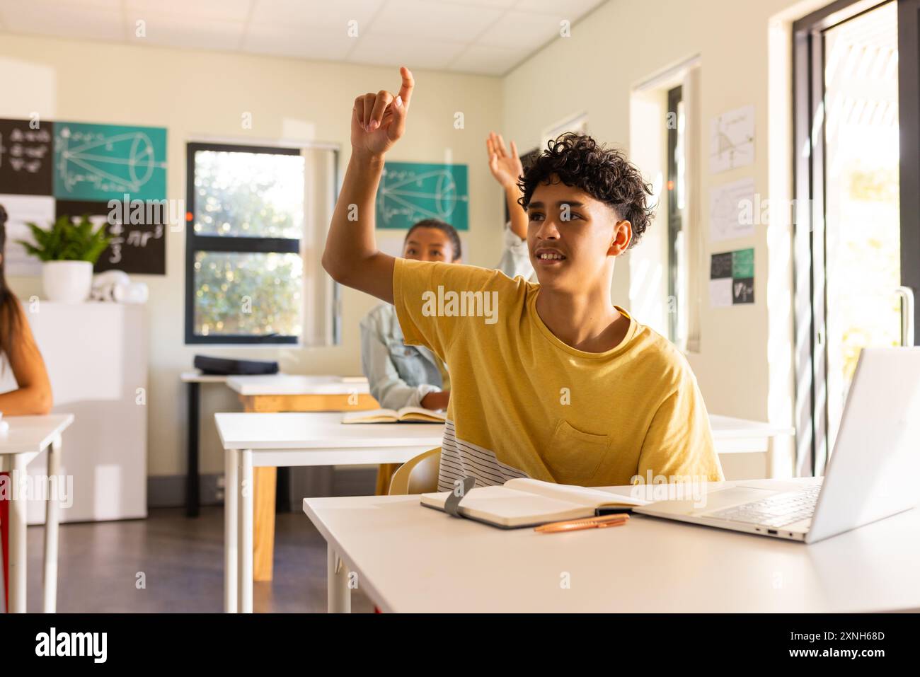 In high school, teenage boy raising hand while sitting at desk with ...