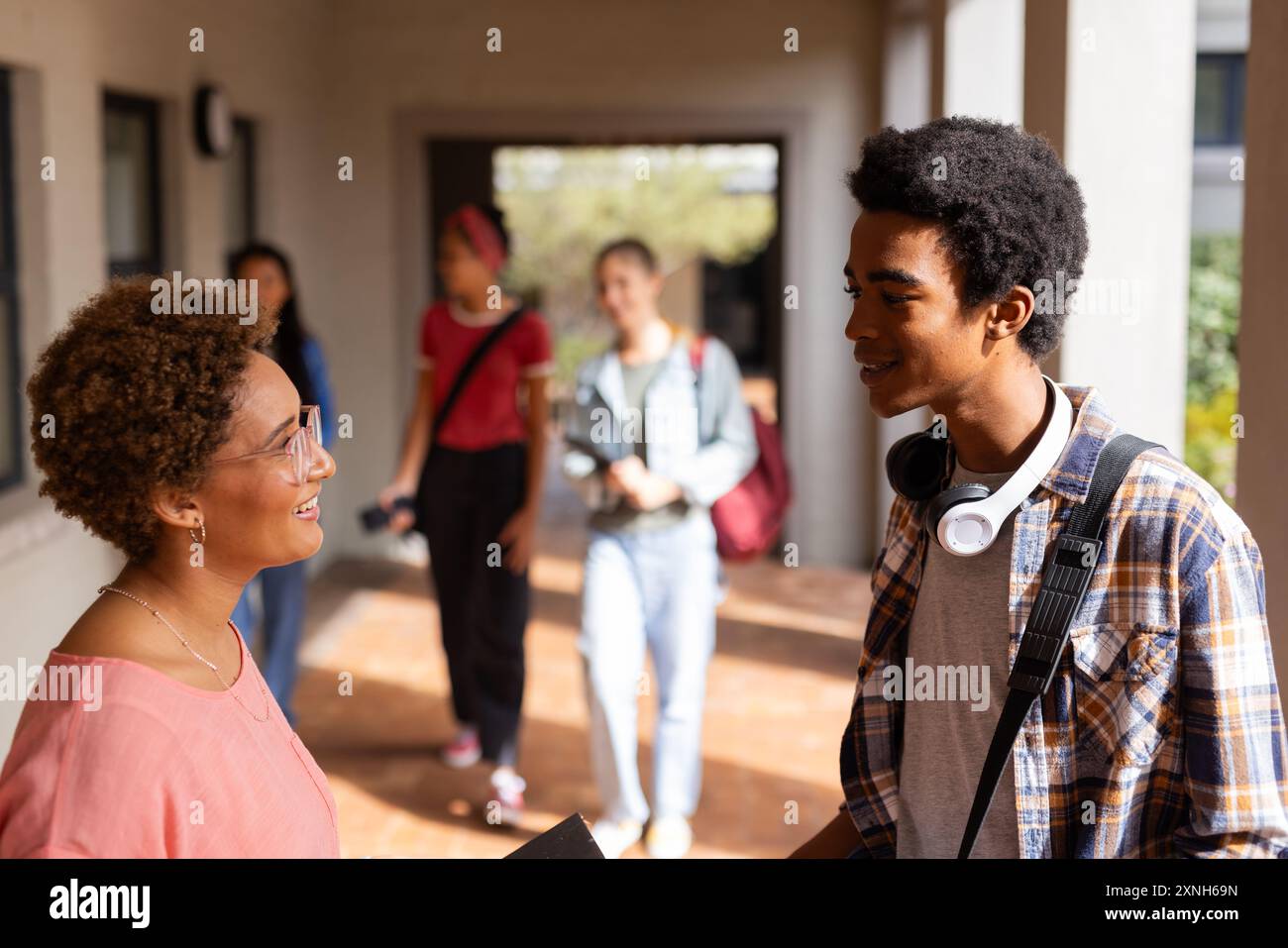 Teacher and student talking in high school hallway, other students walking in background Stock Photo