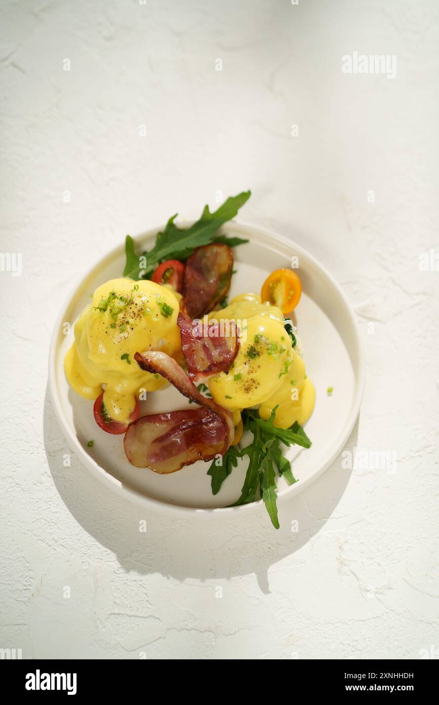 Savory breakfast delight: Eggs Benedict with bacon and fresh herbs Stock Photo