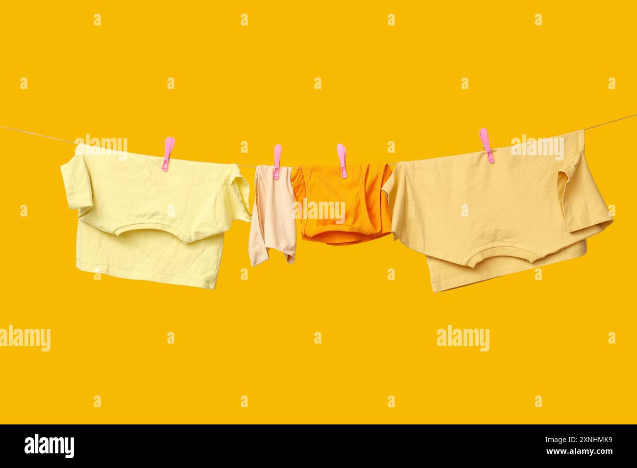 Clean clothes hanging on rope against yellow background Stock Photo - Alamy
