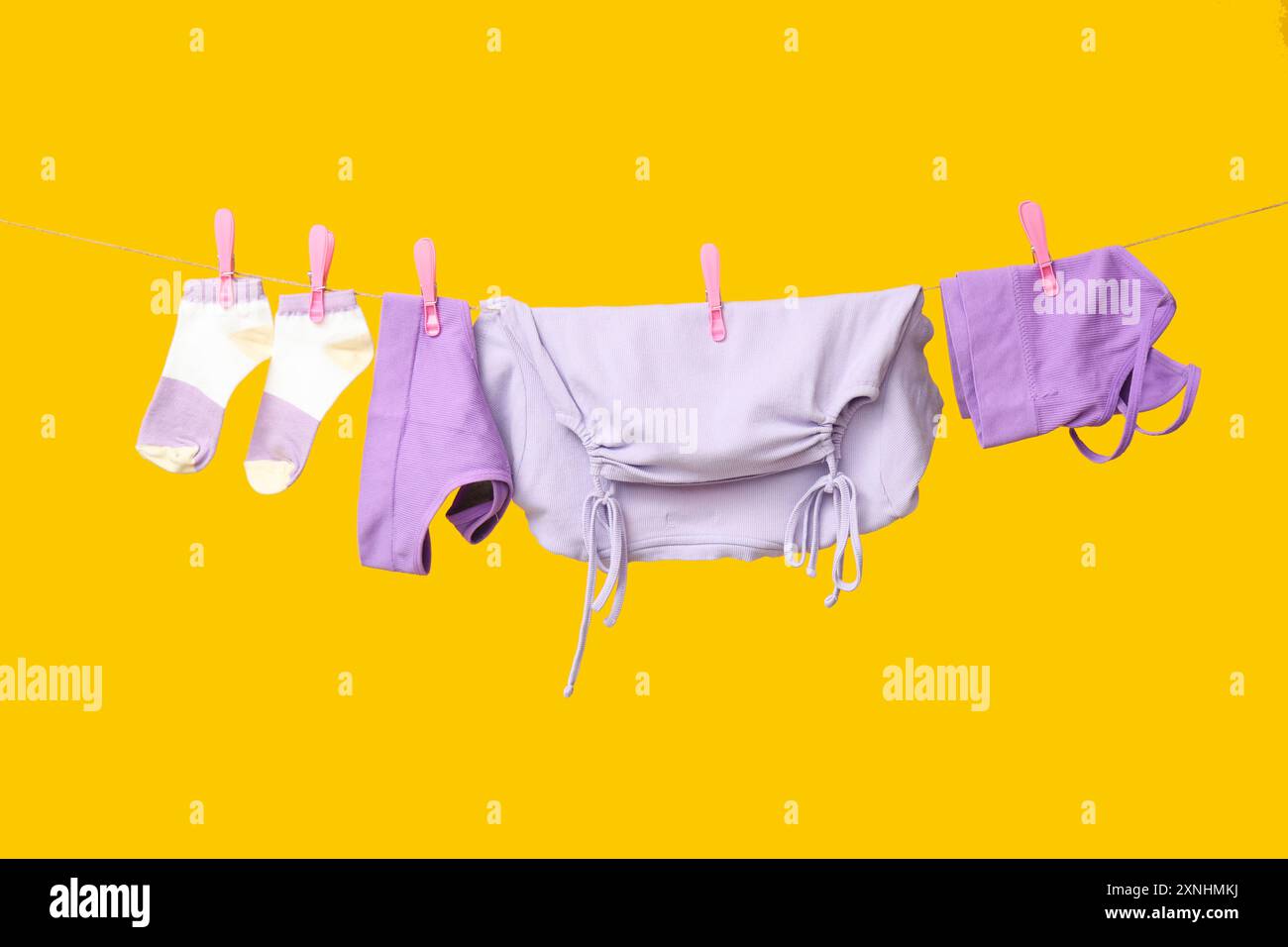 Clean clothes hanging on rope against yellow background Stock Photo - Alamy