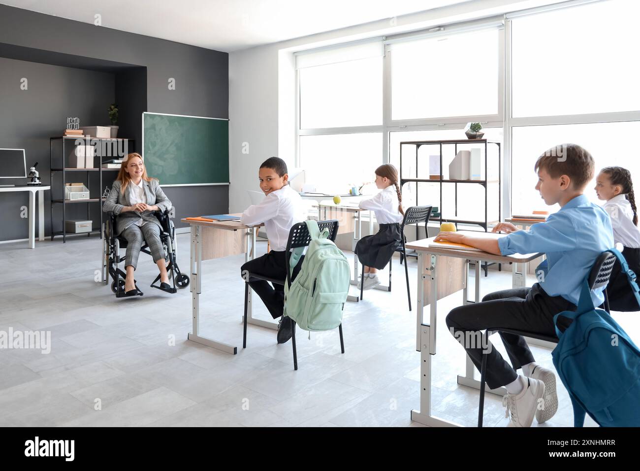 Mature teacher in wheelchair conducting lesson to little pupils at ...