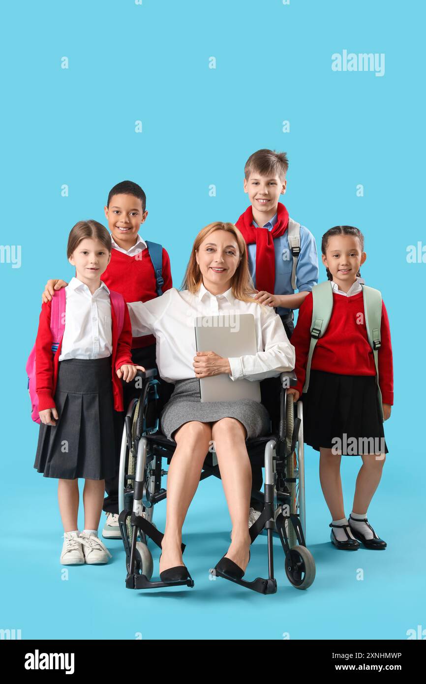 Mature teacher in wheelchair with laptop and little pupils on blue ...
