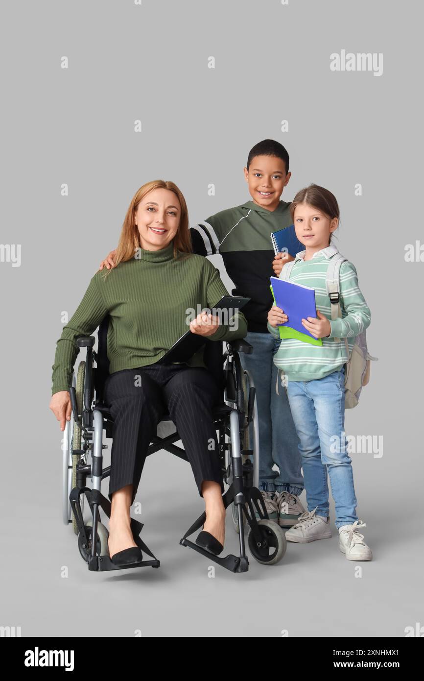 Mature teacher in wheelchair with little pupils on light background ...
