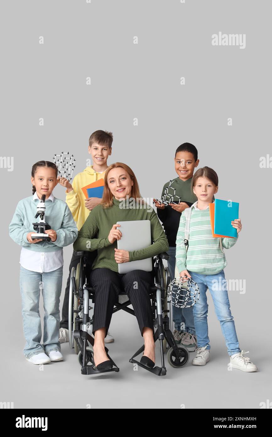 Mature science teacher in wheelchair with laptop and little pupils on ...