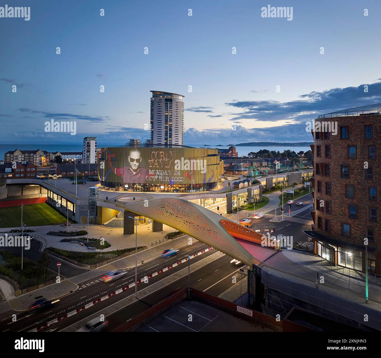 Illuminated bridge and arena at dusk. Swansea Arena  and Copr Bay Bridge, Swansea, United Kingdom. Architect: acme, 2024. Stock Photo