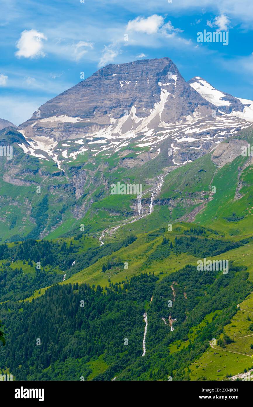 picturesque Austrian mountain scenery with bright green slopes and snow-capped peaks under a bright blue sky. Stock Photo