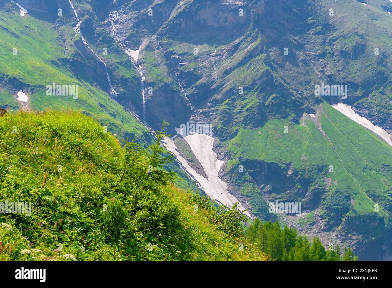 Austrian mountains in Austria with snow-capped peaks and green slopes, streams flowing down from the mountains, against a blue sky with clouds. Stock Photo