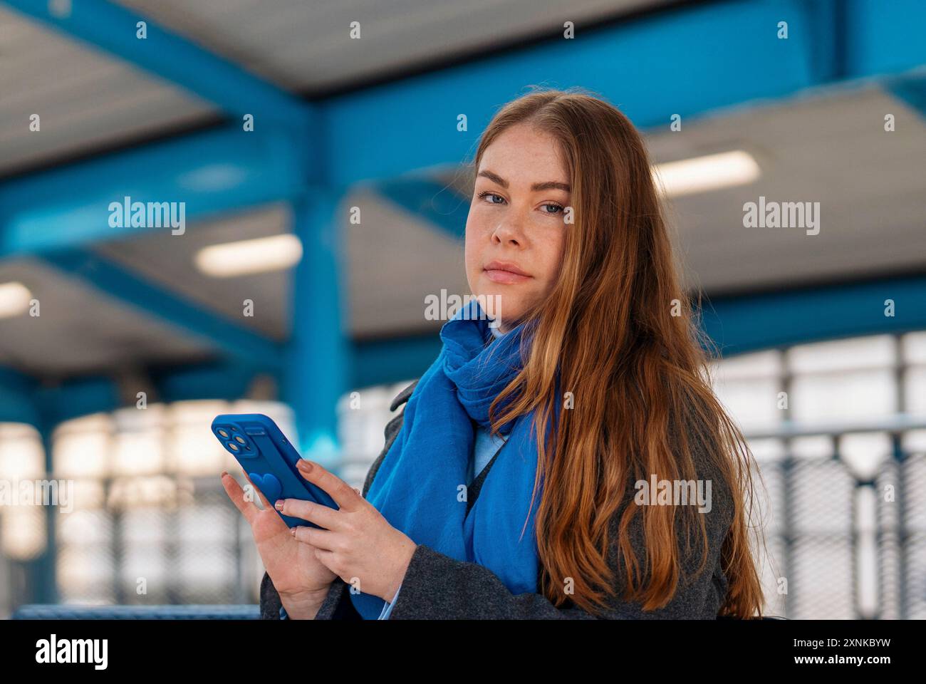 an excited female holding a smartphone while at the train station, airport, bus stop . Safety travel concept Stock Photo