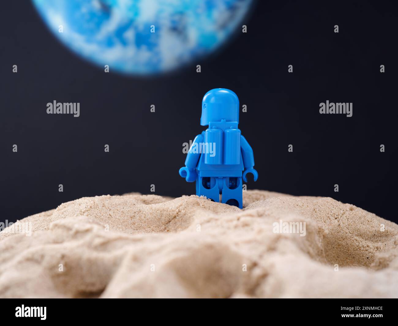 Tambov, Russian Federation - July 28, 2024 Lego astronaut minifigure standing on sand on a planet and looking at another blue planet. Back view. Stock Photo