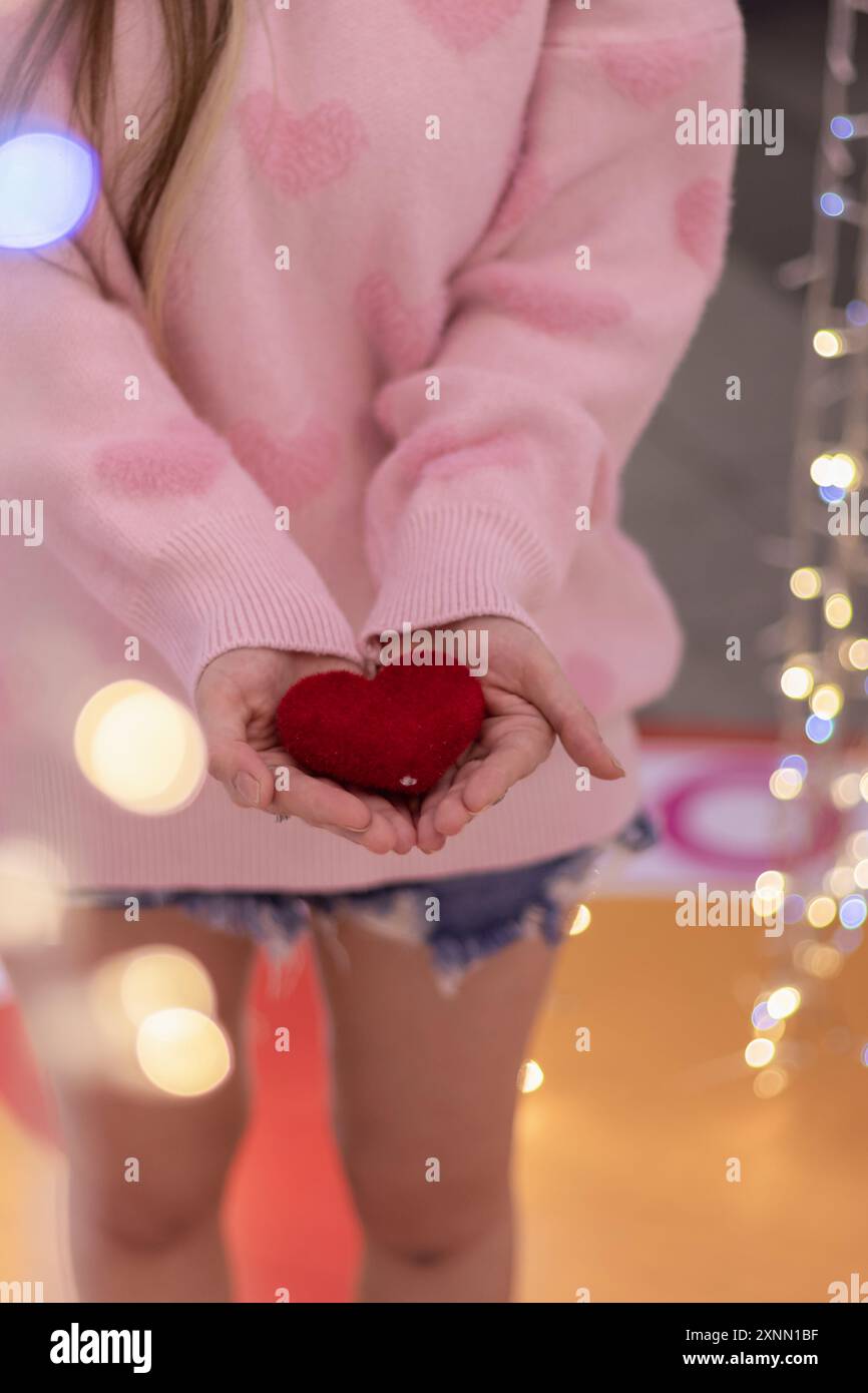 A girl wearing a pink sweater and holding a red heart in her hand on a