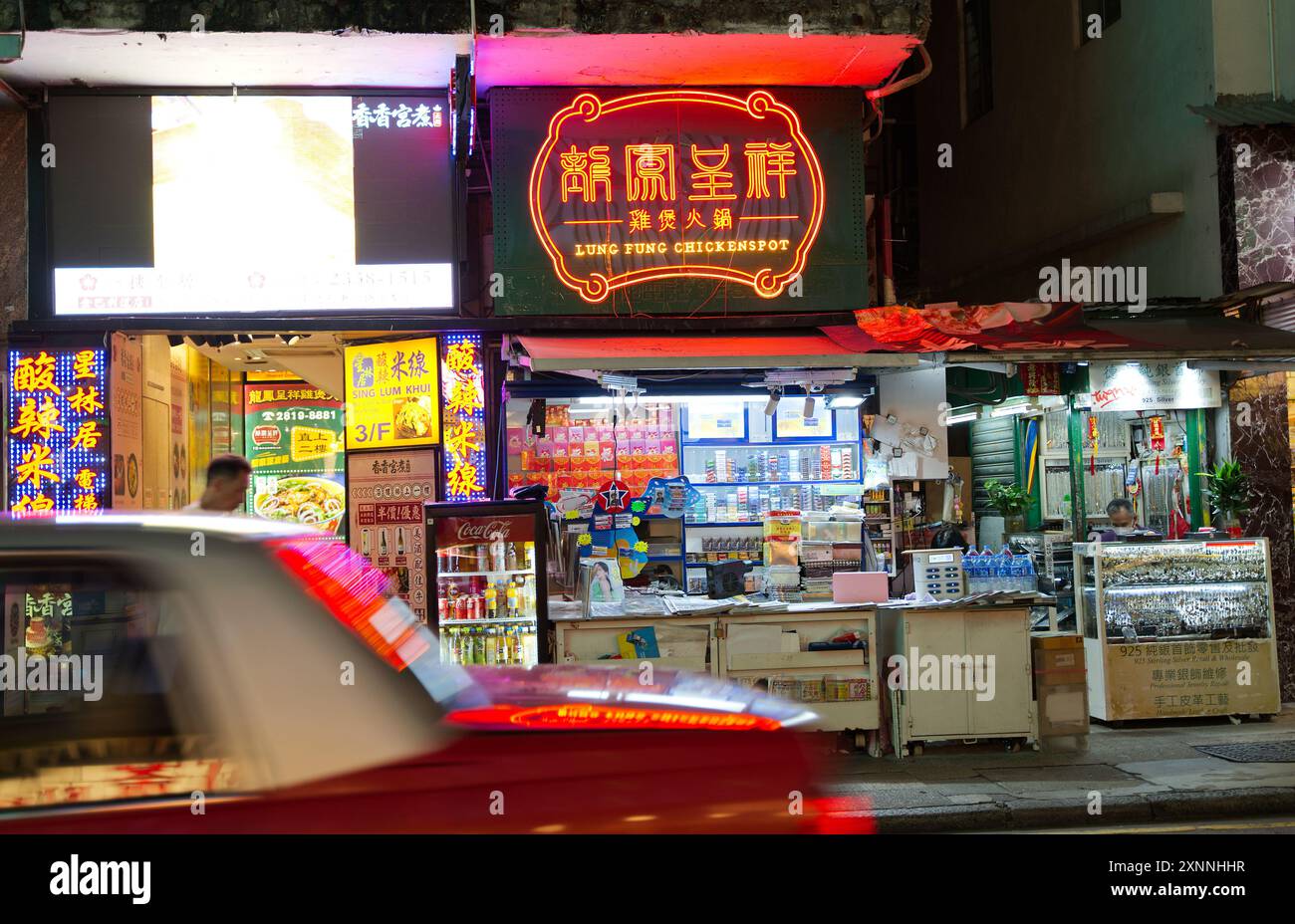 Lung Fung Chicken Shop and restaurant sign at night with a red taxi moving past in the foreground. Hong Kong - 27th May 2024 Stock Photo