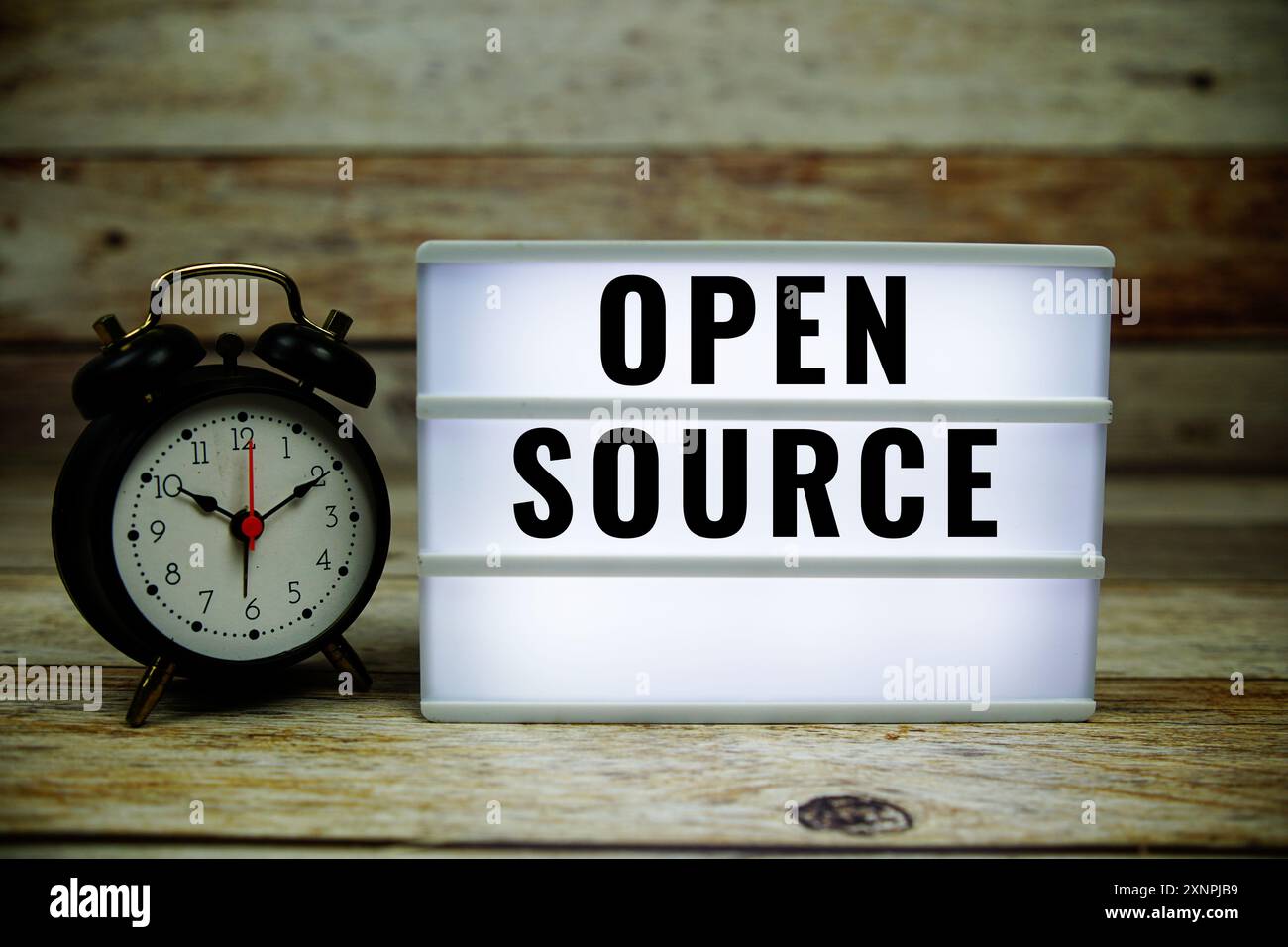 Open Source text on LED lightbox with alarm clock on wooden background Stock Photo
