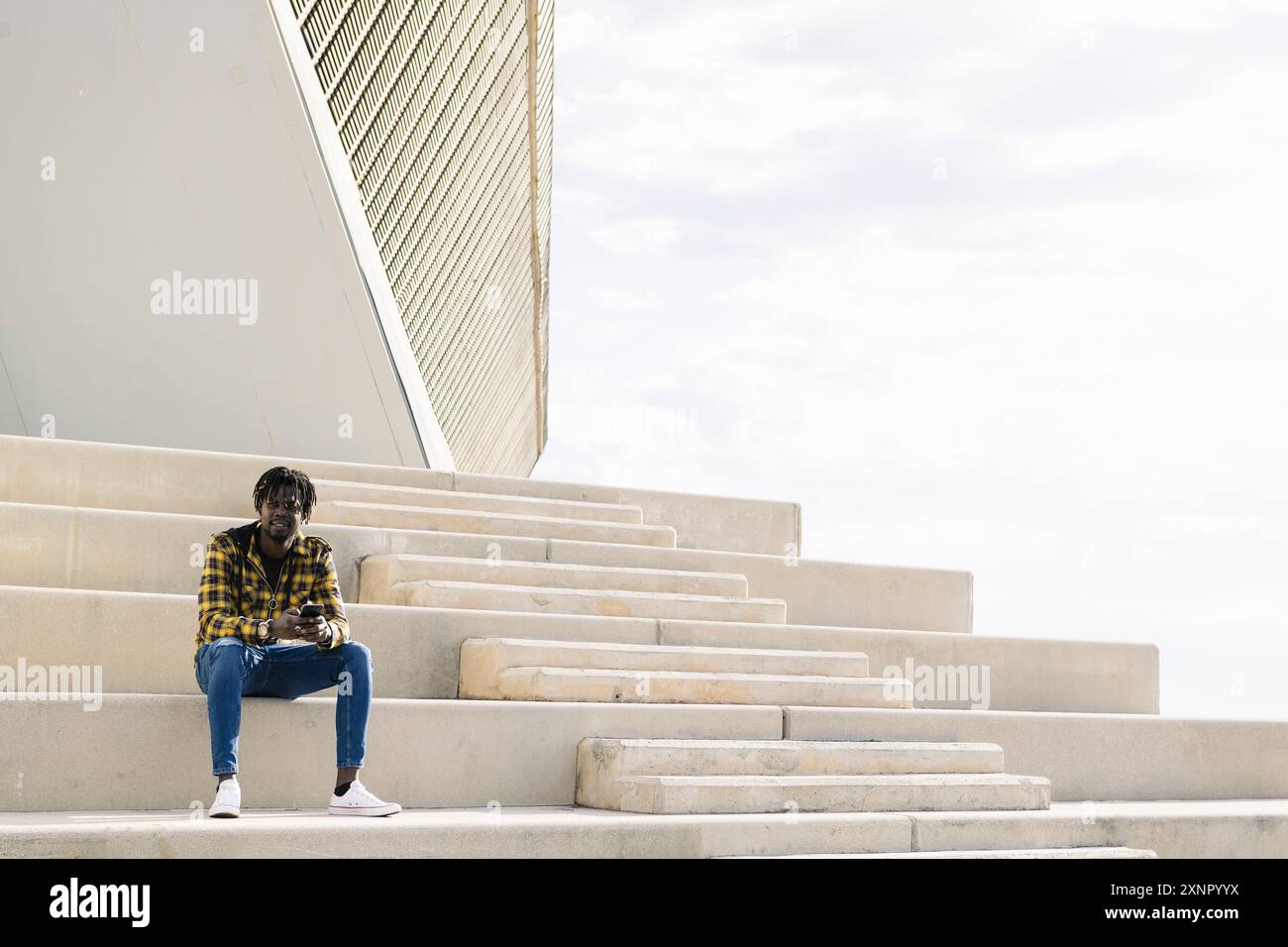 black man sitting on a staircase with his phone Stock Photo
