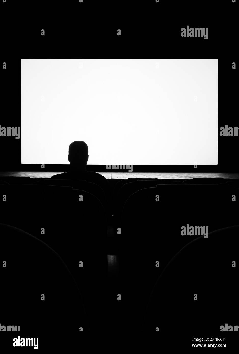 Silhouette of a man, a lone spectator sitting in a chair in the cinema hall against a white screen, rear view black and white photo Stock Photo