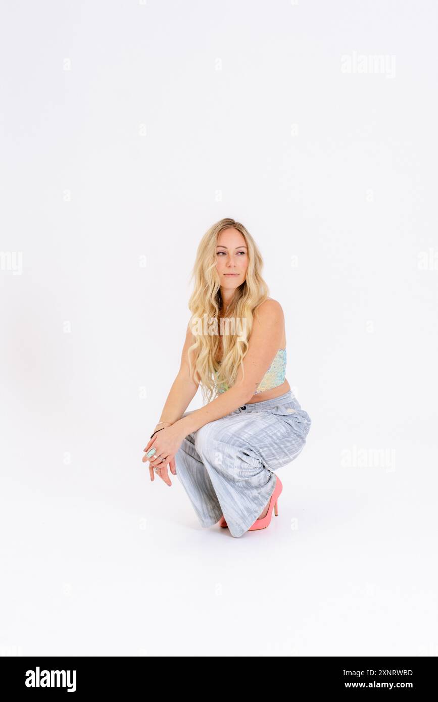 Woman in casual pastel outfit, and pink heels, crouching with a Stock Photo