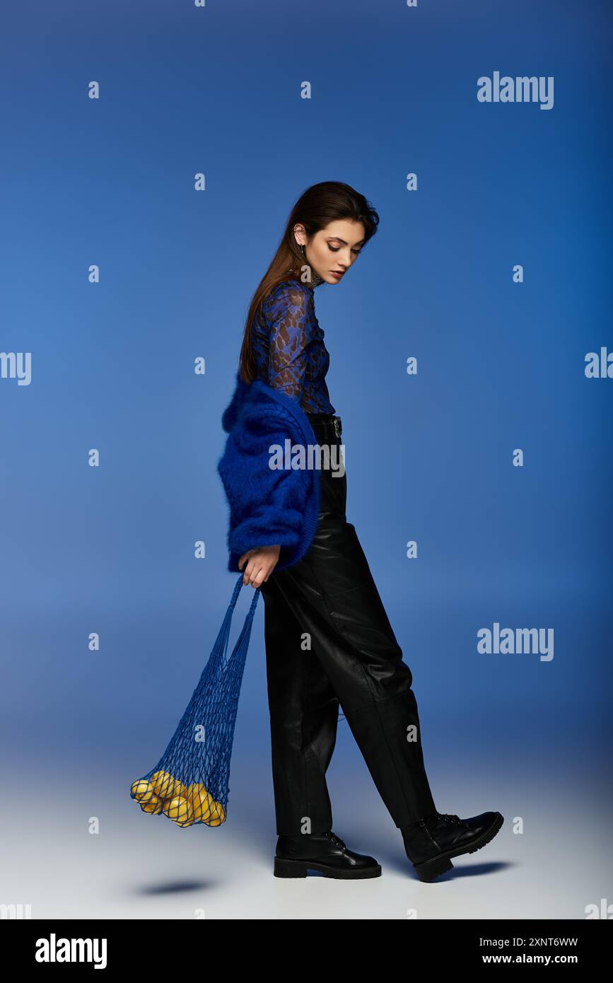 A young woman in a blue coat and black trousers walks with a bag of fruit. Stock Photo