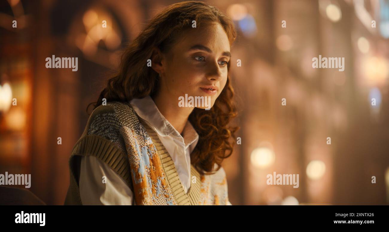 Serene Young Woman in a Cozy Sweater, Engaged in Thoughtful Contemplation in a Warmly Lit Vintage Library. Her Curly Hair and Gentle Smile Add to the Peaceful Ambiance of the Scene. Stock Photo