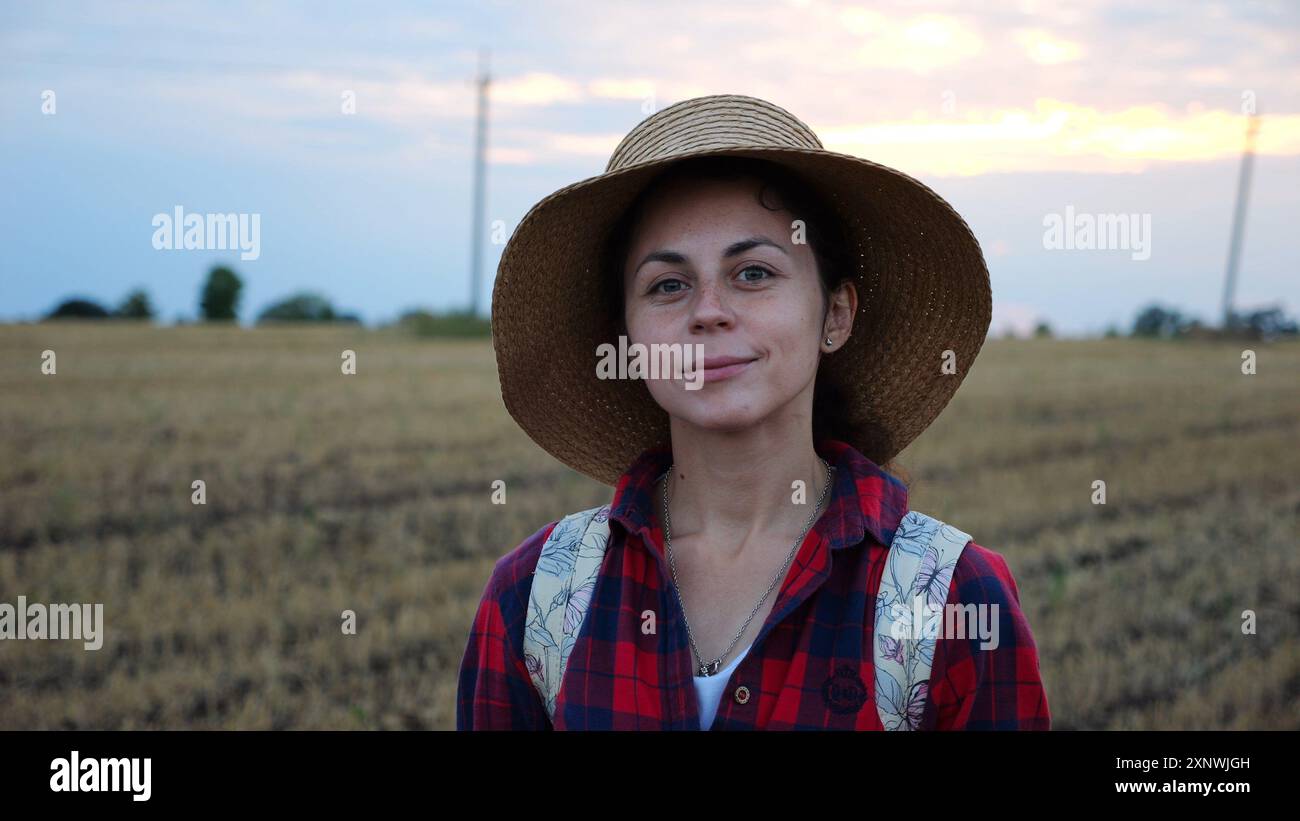 Happy smiling female farmer looks into camera standing at wheat field ...