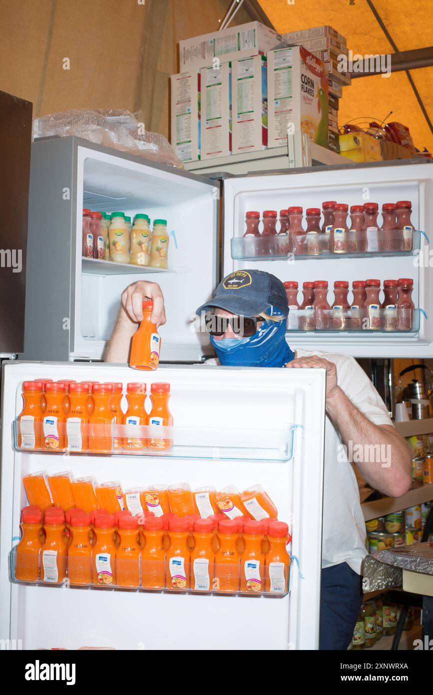 A man wearing a cap and scarf is reaching into a refrigerator filled with orange juice bottles ...
