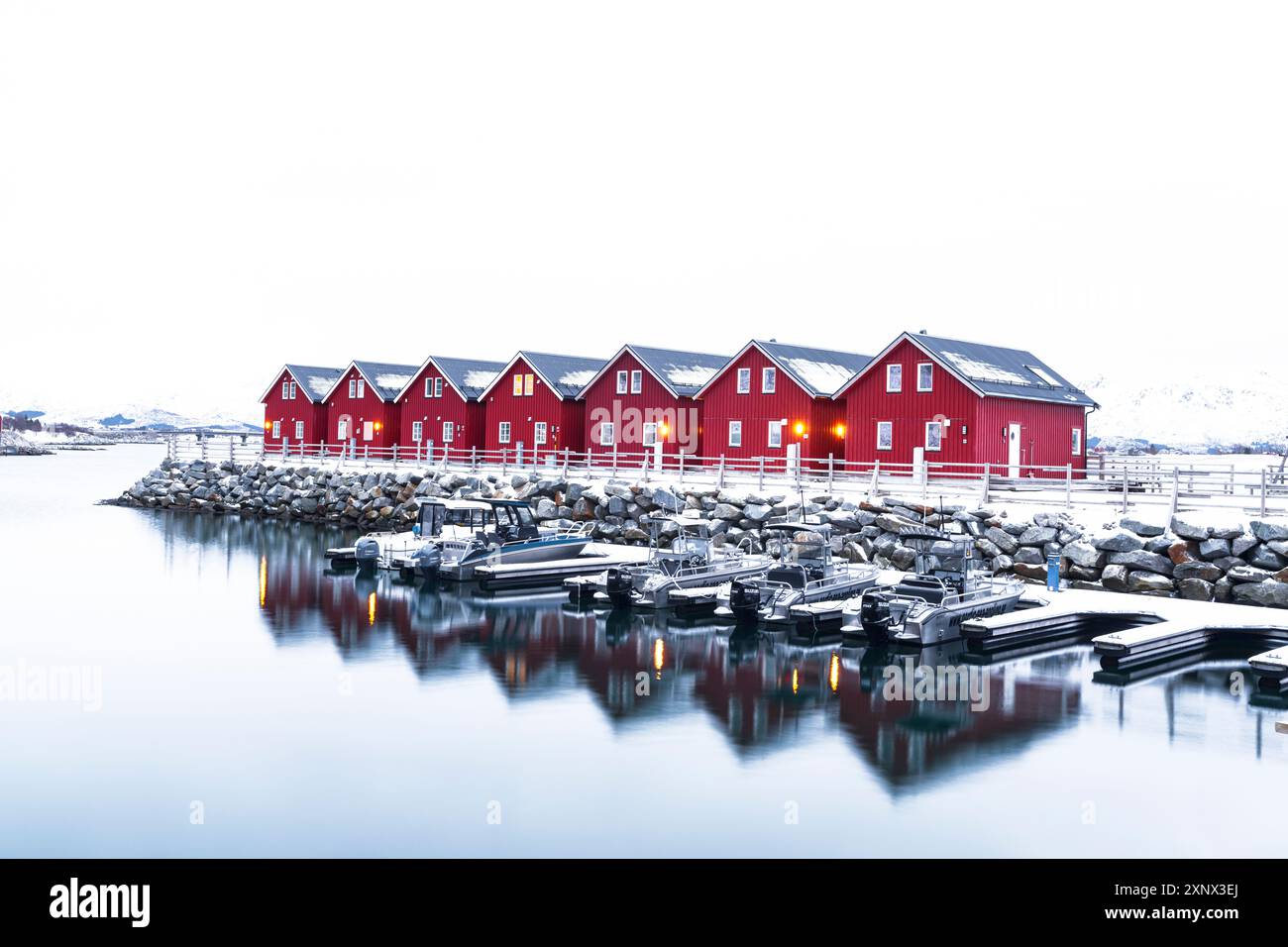 Row Of Red Traditional Wooden Cabins Standing Above A Small Harbour In row-of-red-traditional-wooden-cabins-standing-above-a-small-harbour-in