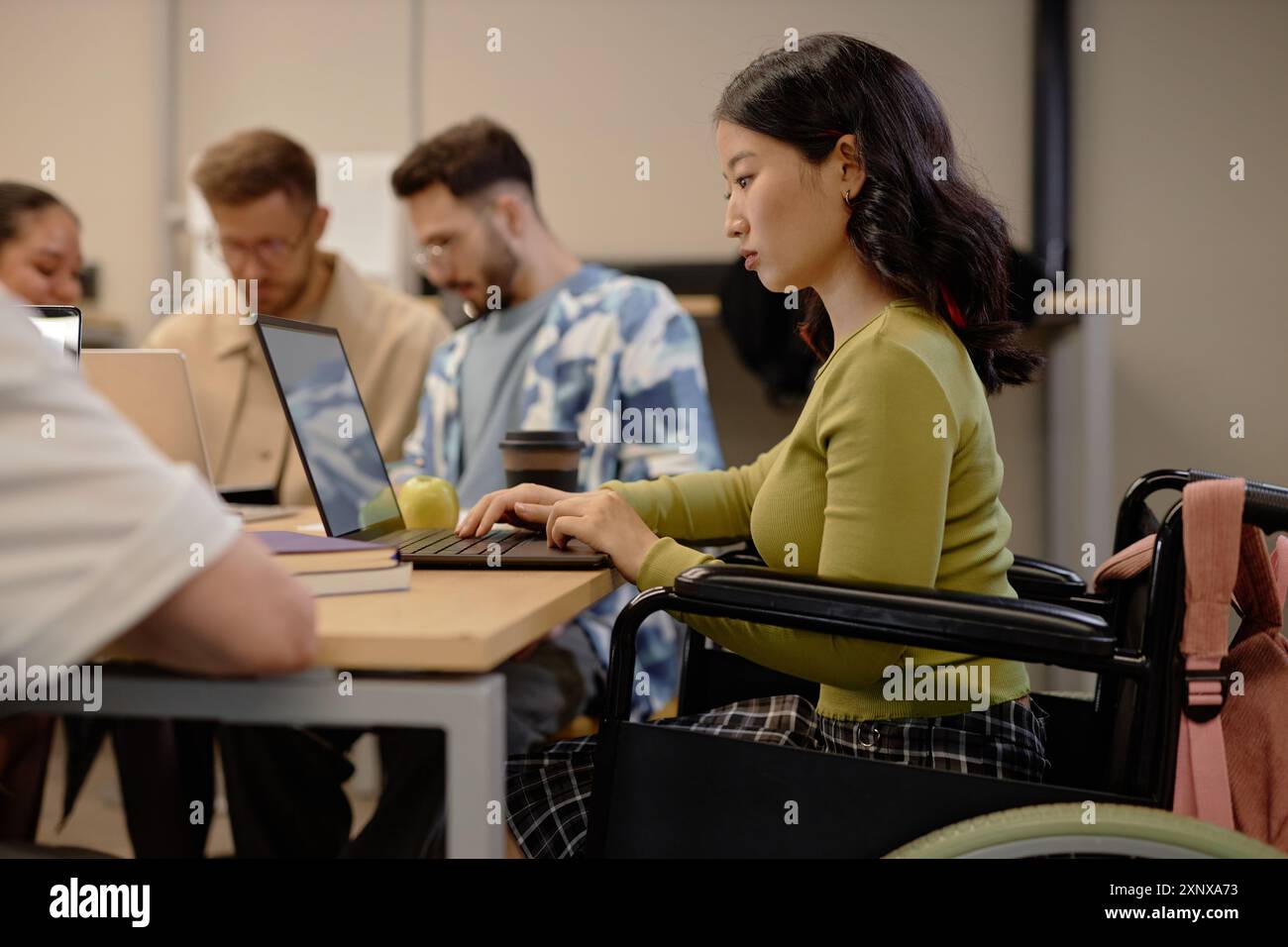 Side view of focused Asian female wheelchair user working on laptop at ...