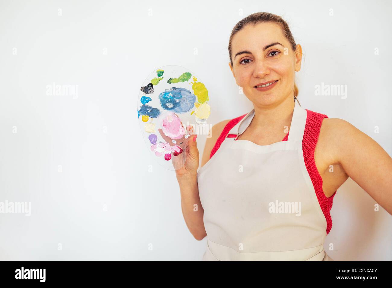 A young woman smiles and holds a palette of paints. A charming artist ...