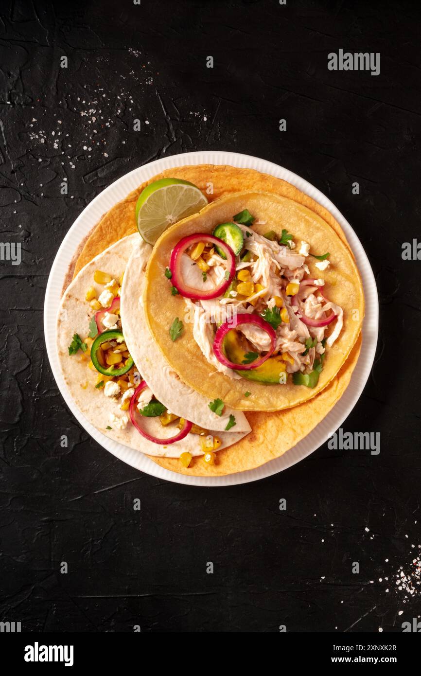 Tacos, tortillas with chicken meat, avocado, maize, and onion, top shot on a dark background Stock Photo