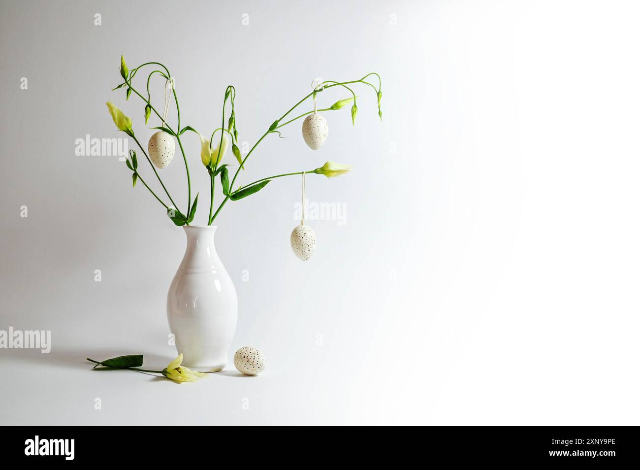 Delicate flower bunch in a white vase decorated with hanging Easter eggs on a light gray background, copy space, selected focus, narrow depth of field Stock Photo