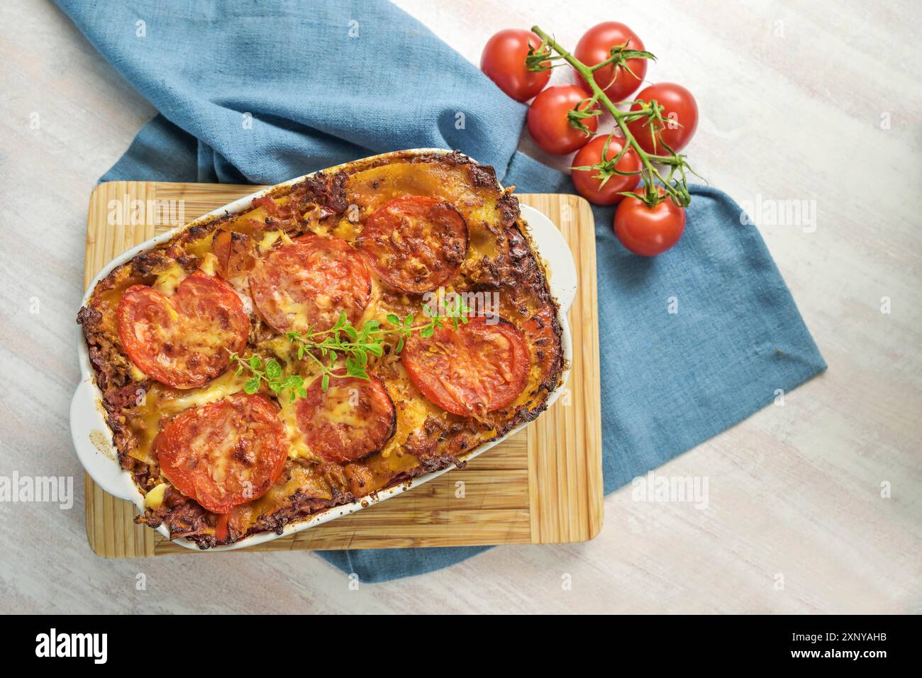 Lasagna, casserole with layered pasta, Bolognese beef sauce, vegetables and tomatoes, topped with melted cheese on a wooden kitchen board and a blue Stock Photo