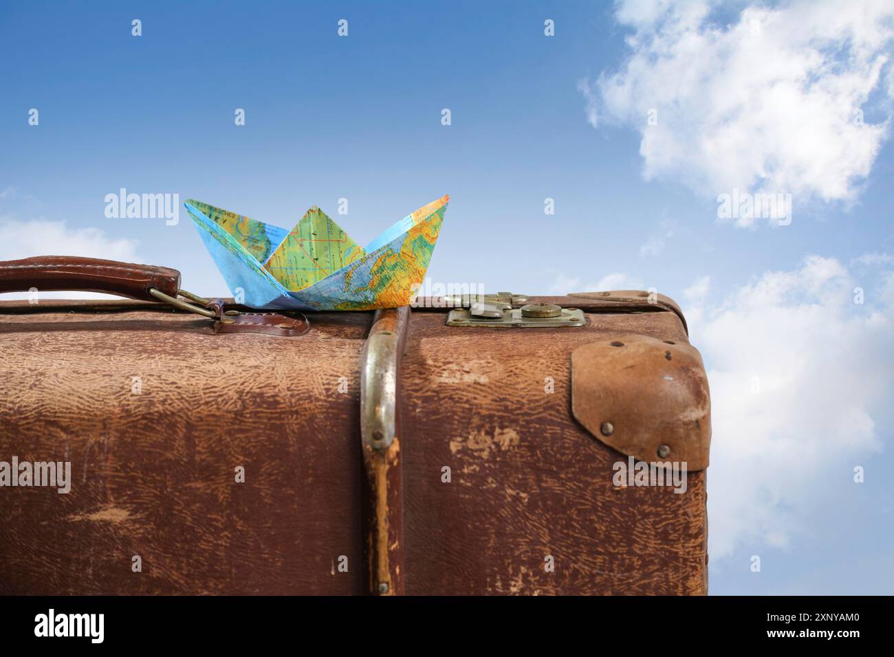 Paper boat folded from a map on an old vintage suitcase against a blue sky with white clouds, wanderlust, cruise and travel concept, copy space Stock Photo
