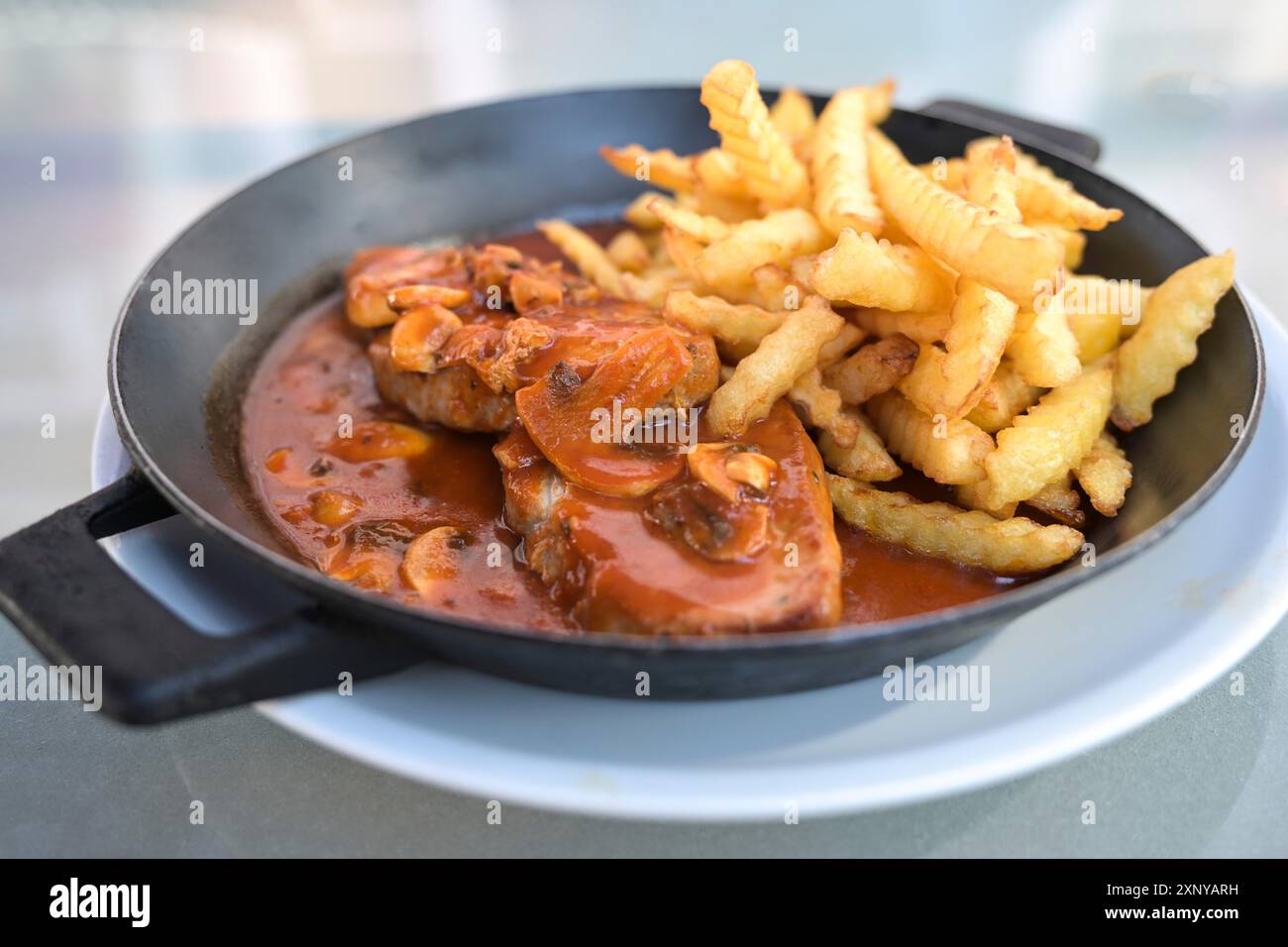 Pork steak with mushroom sauce and fries served in an iron pan, meal with meat for lunch or dinner, selected focus, narrow depth of field Stock Photo