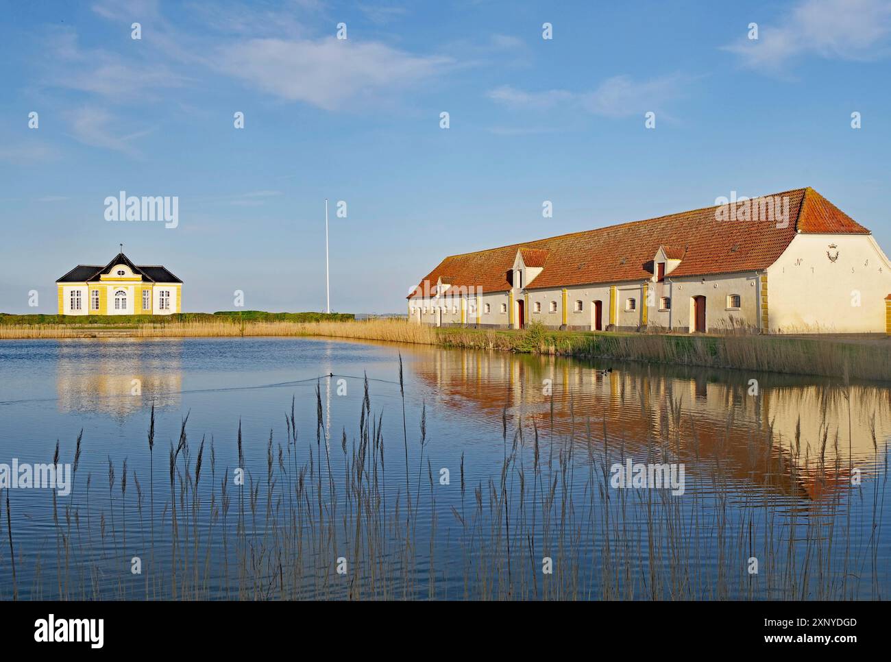 Building and house by the lake with reflection in the calm water under a blue sky, Valdemars Slot, Tasinge, Manor Route, Denmark Stock Photo