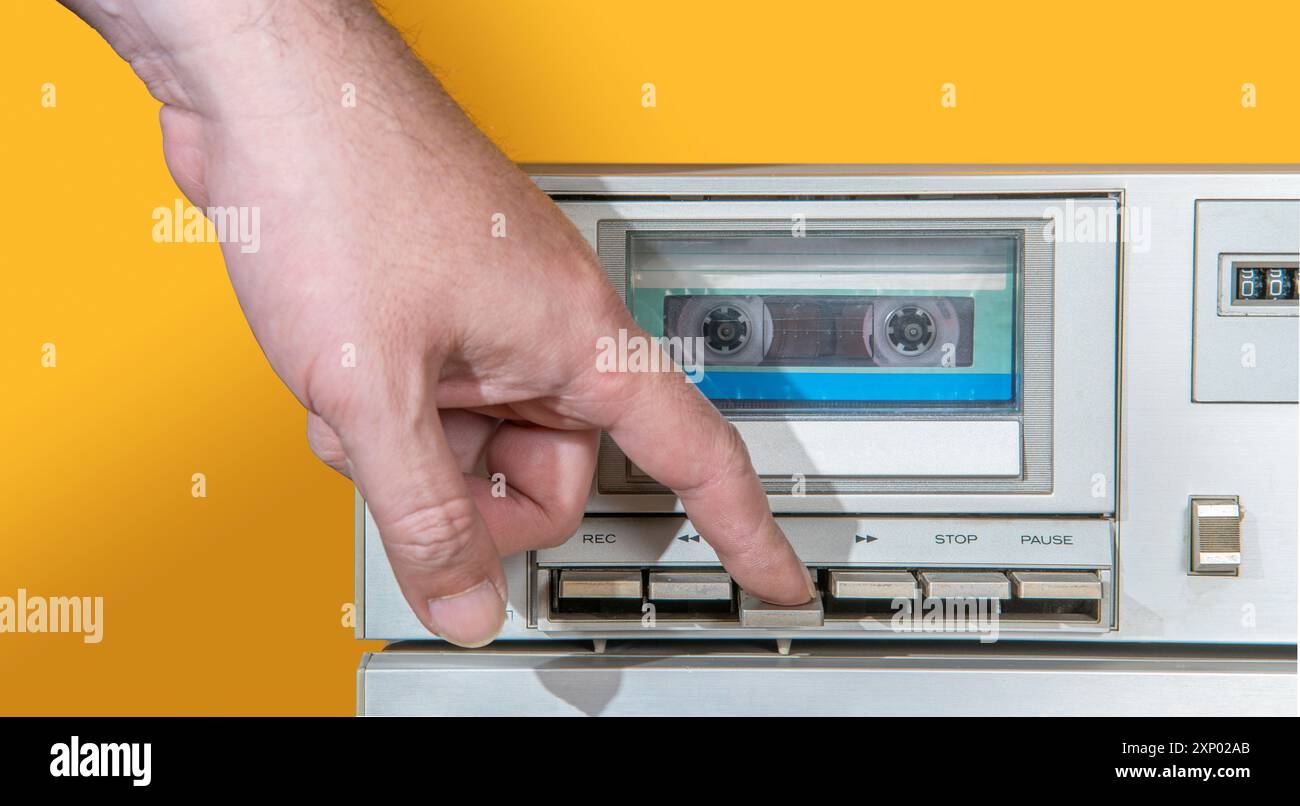 Front view of man's hand crushing the key of old aluminum recorder with music cassette inside against yellow background Stock Photo