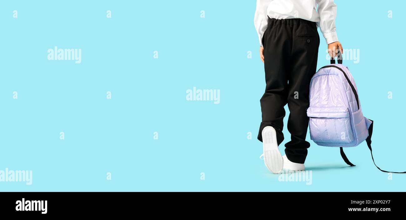 Little schoolboy with backpack walking on blue background, back view ...