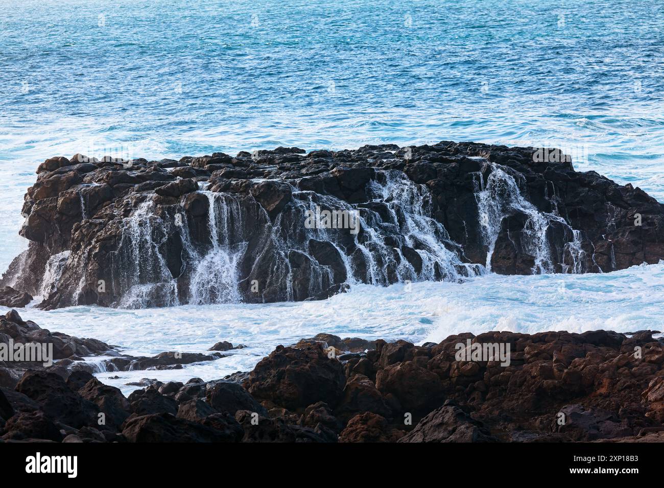 Massive rock formation in an ocean. Sea water is choppy, and the rocks ...