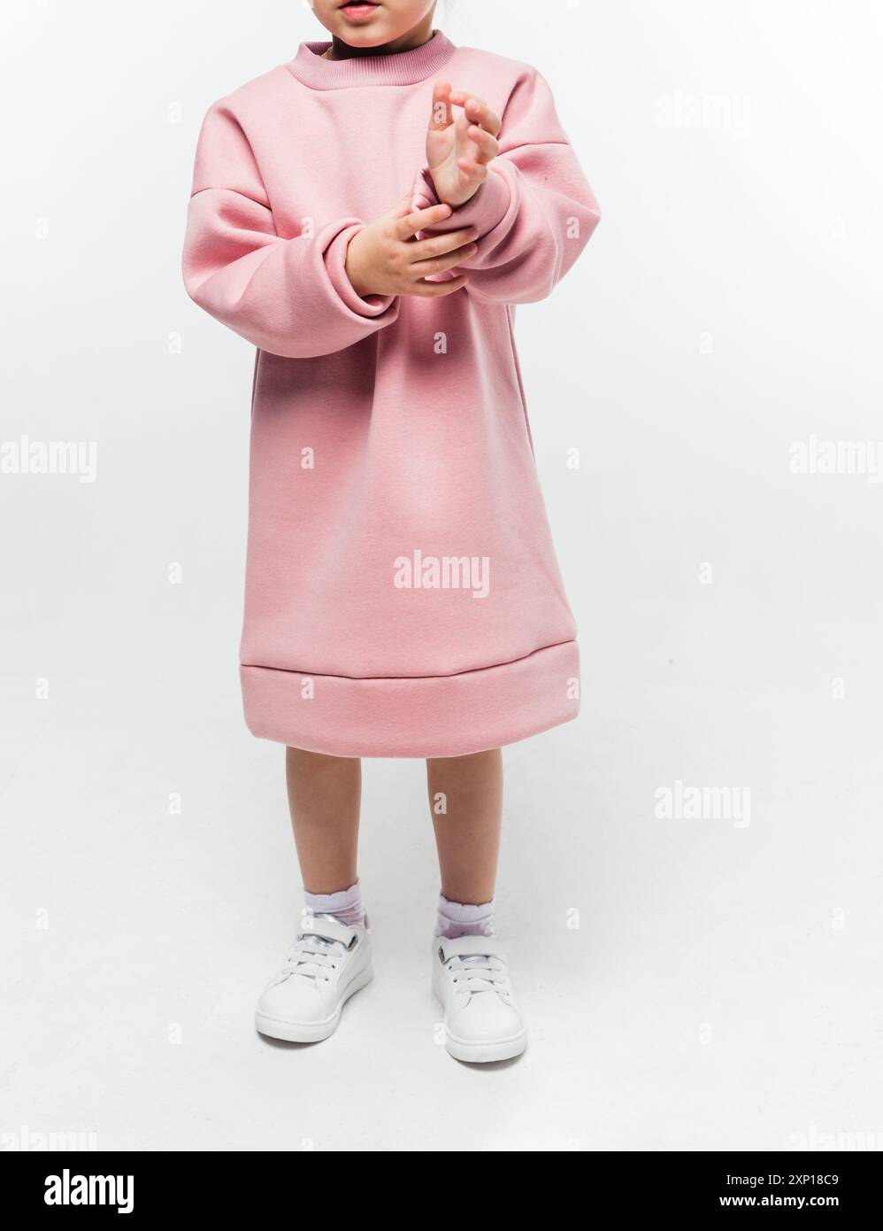 A girl wearing a pink oversized dress with long sleeves, adjusting her sleeve. Vertical photo. Stock Photo