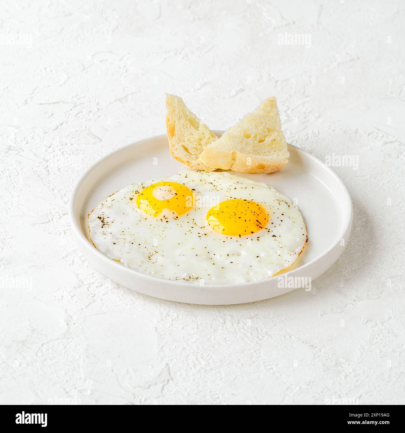 Two perfectly fried eggs with crispy bread on a white plate Stock Photo